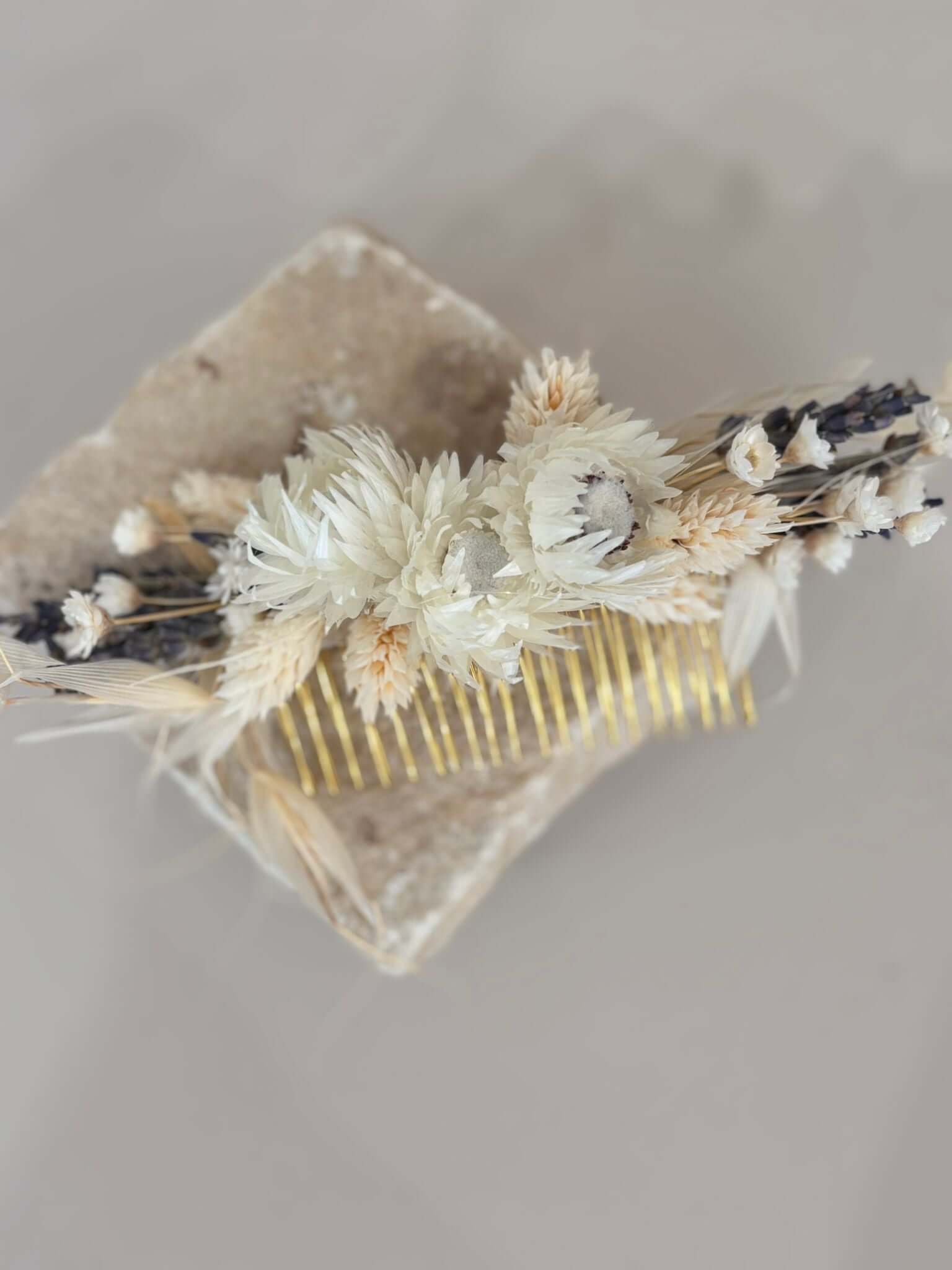 Haarkamm in Beige-Weiß mit Trockenblumen und Lavendel für eine Boho-Hochzeit, auf Steinunterlage präsentiert.