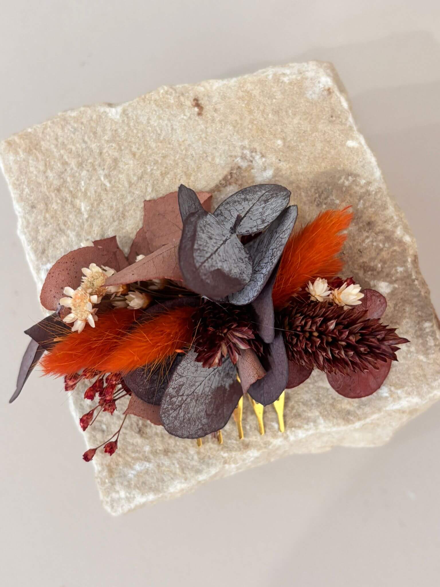Handcrafted haarkamm featuring eucalyptus and dried flowers in deep red and earthy tones on a stone background.
