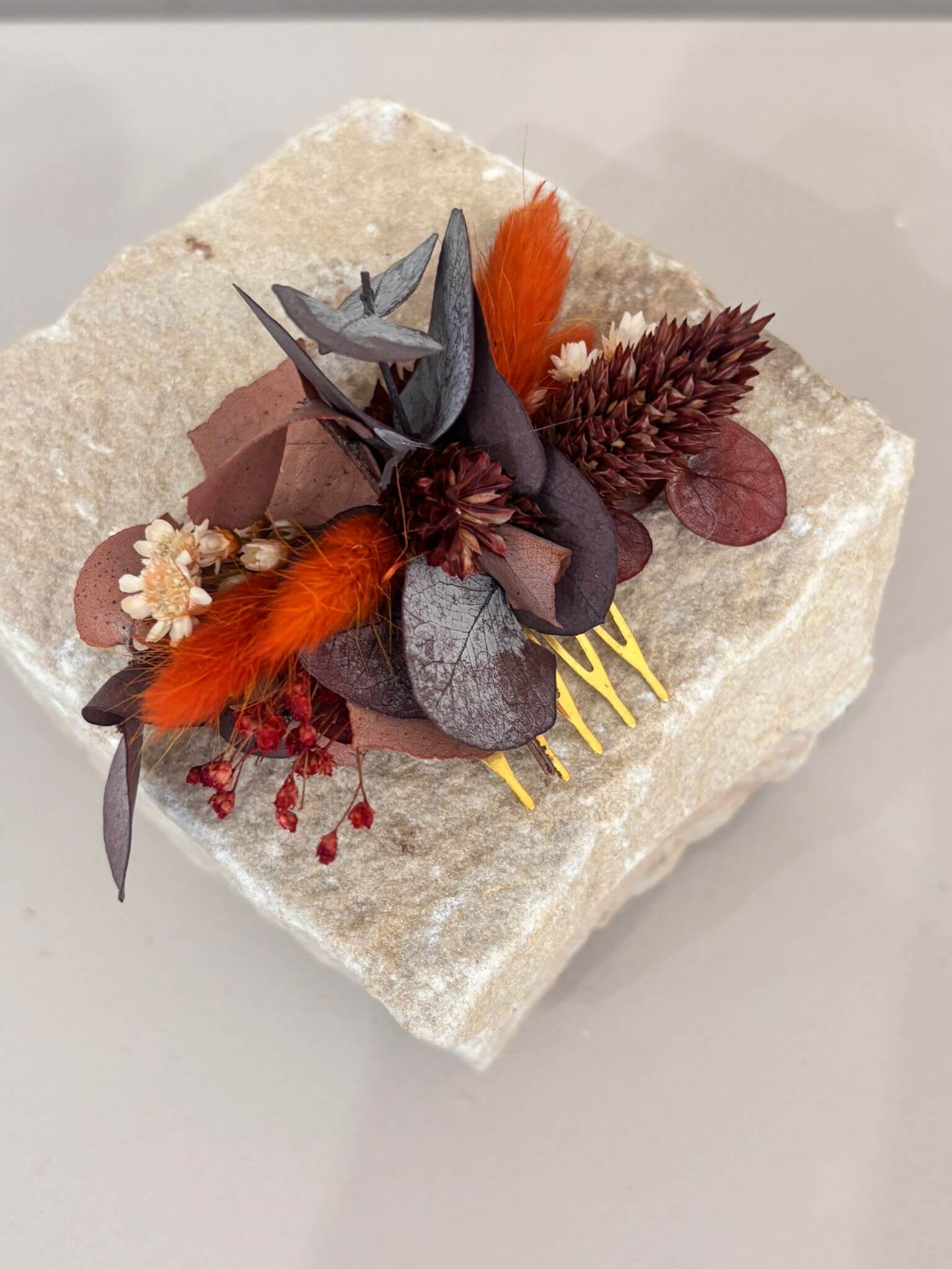 Eukalyptus Haarkamm mit getrockneten Blumen in Rot- und Brauntönen, dekoriert auf einem Stein.