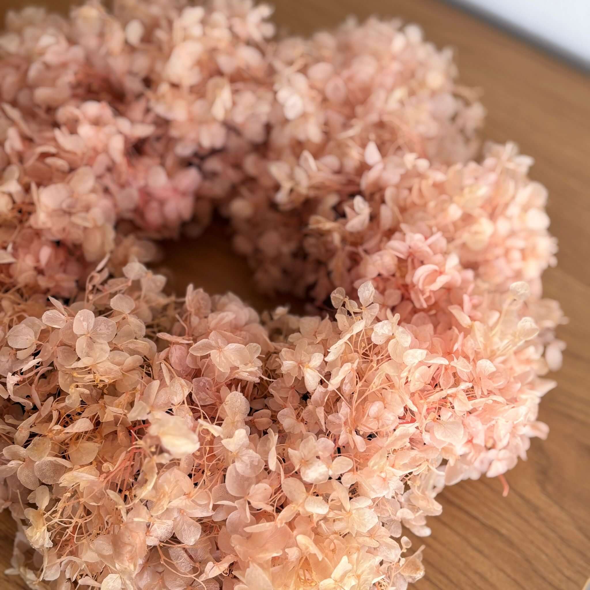 Puristischer Trockenblumenkranz aus rosefarbenen Hortensien auf Holzoberfläche.