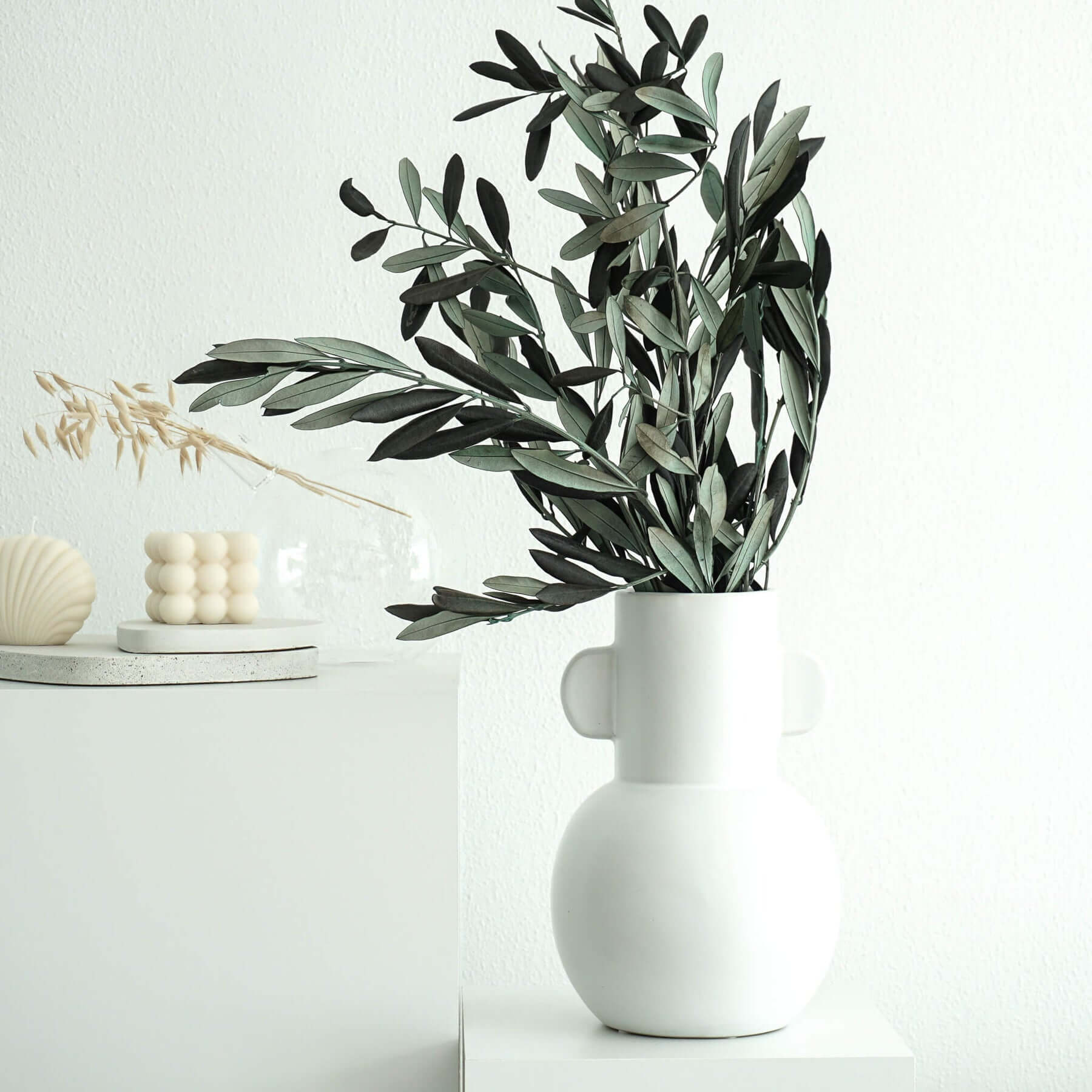 White vase with olive branches and minimalist decor on a light background.