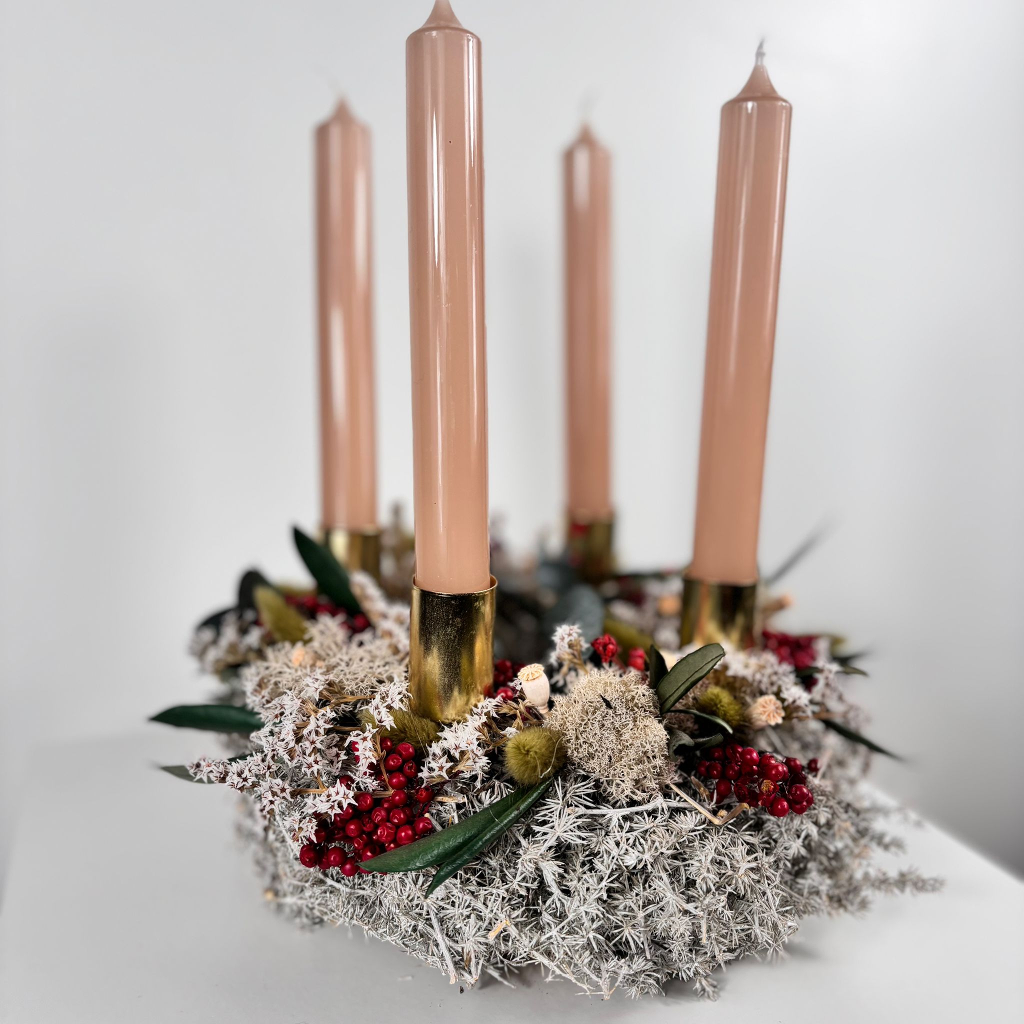 Elegant holiday wreath with four pink candles, adorned with greenery and festive decorations. Perfect for seasonal decor.