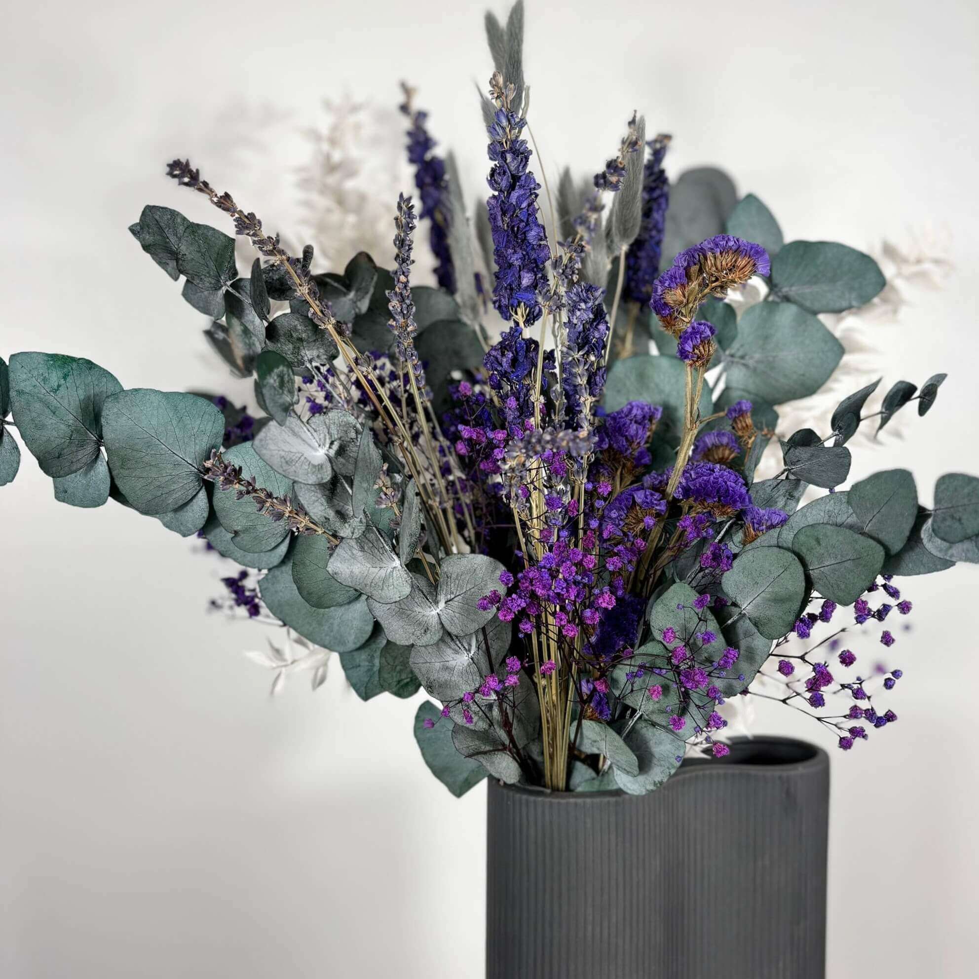 Dried flower bouquet featuring purple blooms and eucalyptus in a modern gray vase. Perfect for home decor.