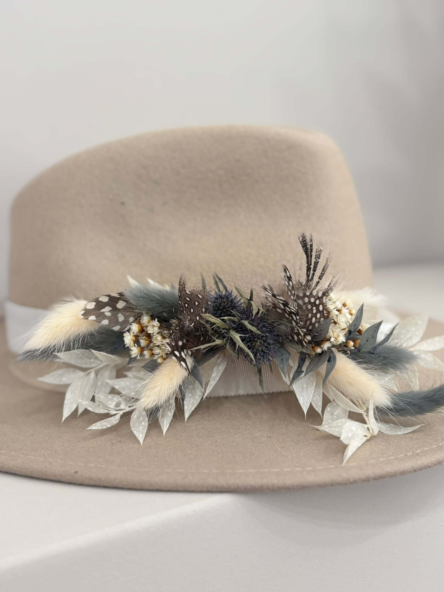 Beige hat adorned with decorative feathers and flowers, showcasing a stylish and unique design.